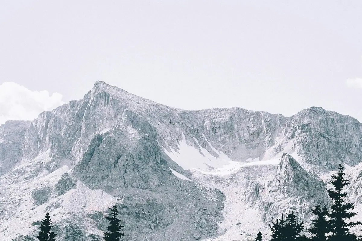 Snow-streaked granite peak above a dark spruce forest
