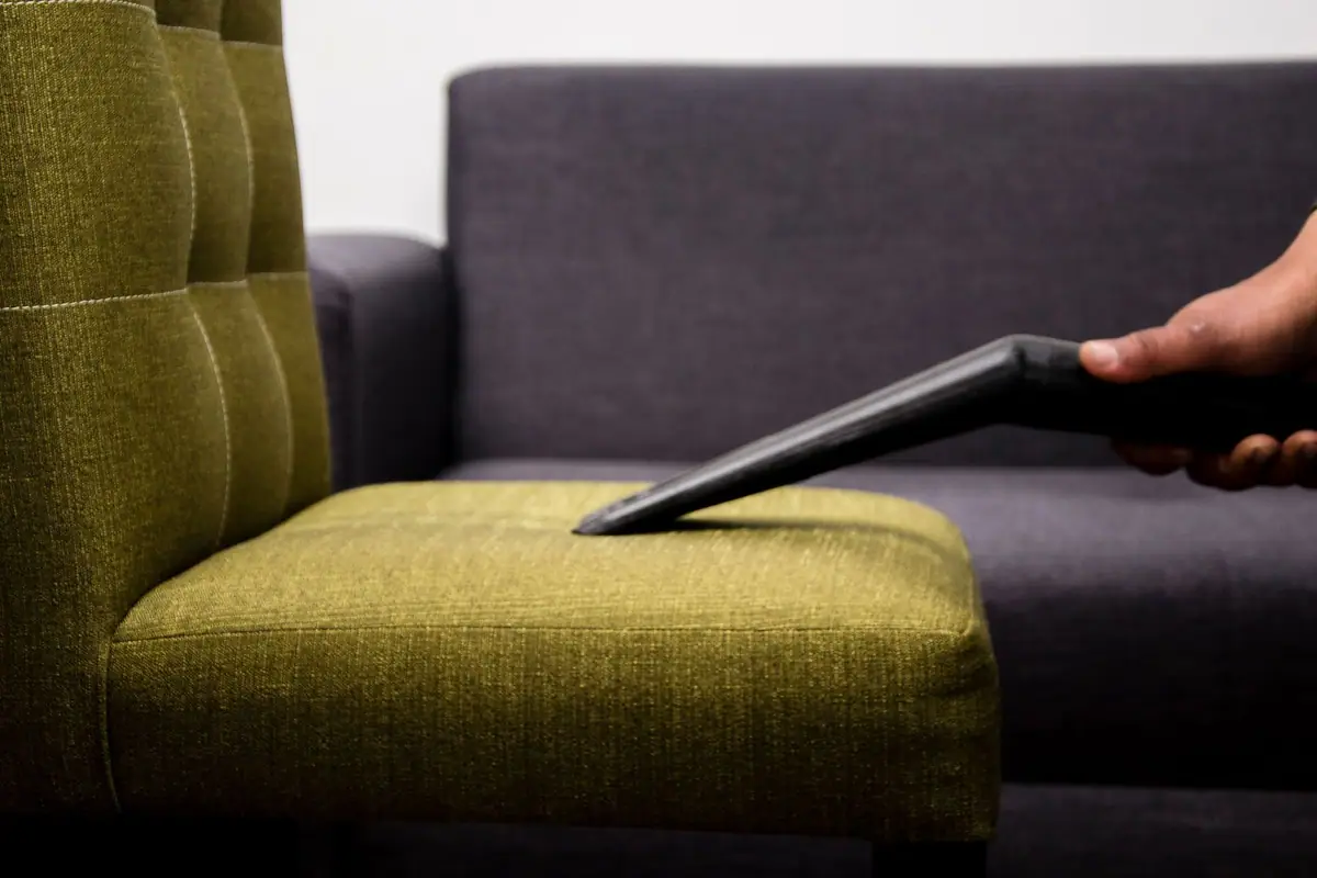 Upholstery tool cleaning the seat of an olive green armchair