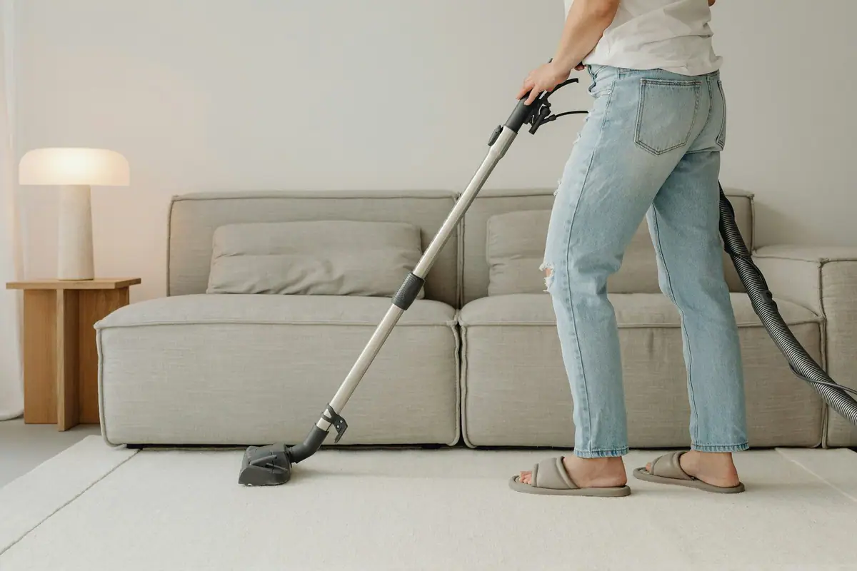 Person vacuuming a cream area rug in a bright living room with a linen sofa