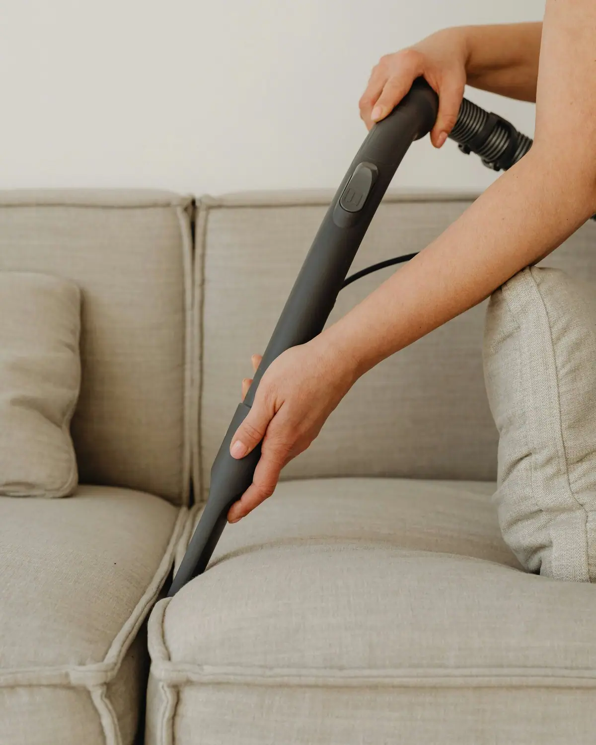 Hands cleaning between the cushions of a beige linen sofa